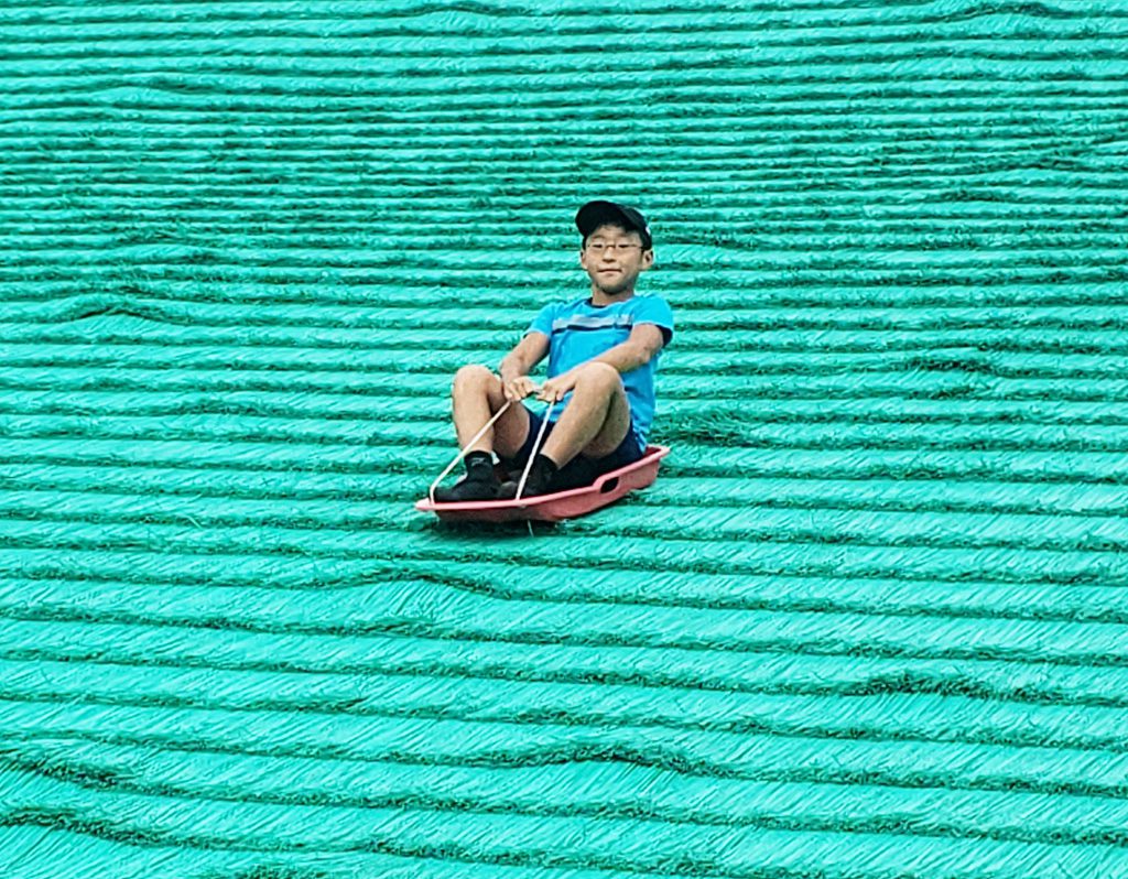 ソリで人工芝を滑る子ども／舎人公園（東京都/足立区）