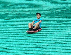 ソリで人工芝を滑る子ども／舎人公園（東京都/足立区）