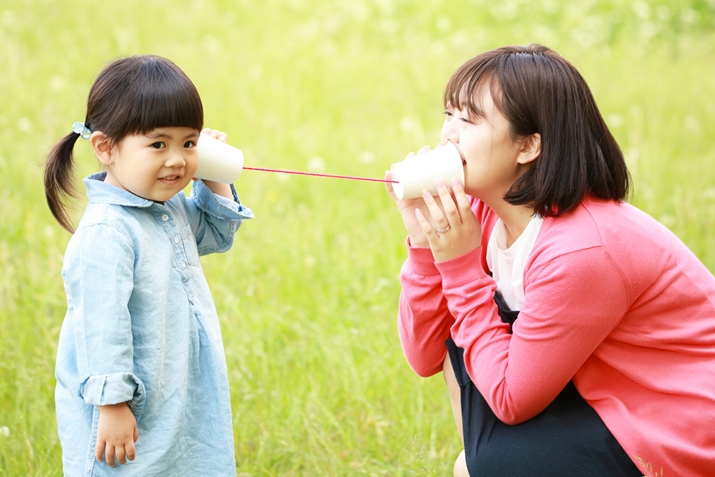 おうちで作った糸電話を外で試してみる親子