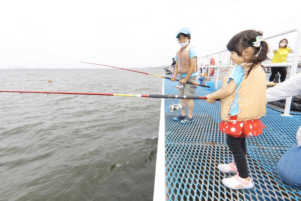 「自分で釣り竿を持ちたい!」 と頑張る4歳。親は後ろからフォローを。